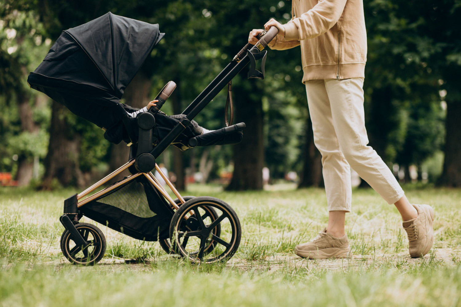 Person schiebt schwarzen Kinderwagen im Park auf Grasweg bei grünen Bäumen