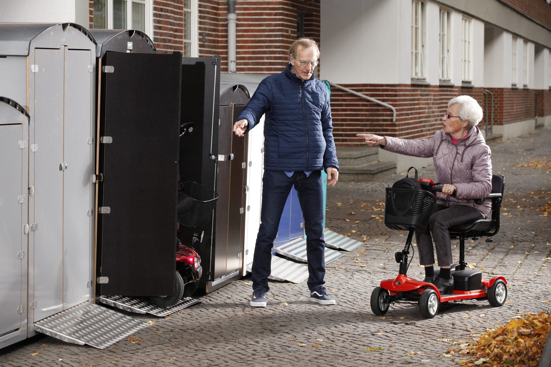 Seniorin auf rotem Elektrorollstuhl spricht mit Mann vor mobilen Rollstuhlgaragen im Herbst