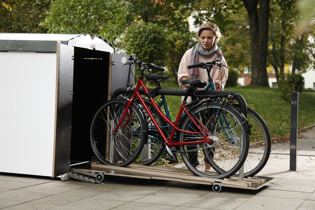 Frau sichert Fahrräder an mobiler Fahrradbox aus Holz im Park bei Bäumen