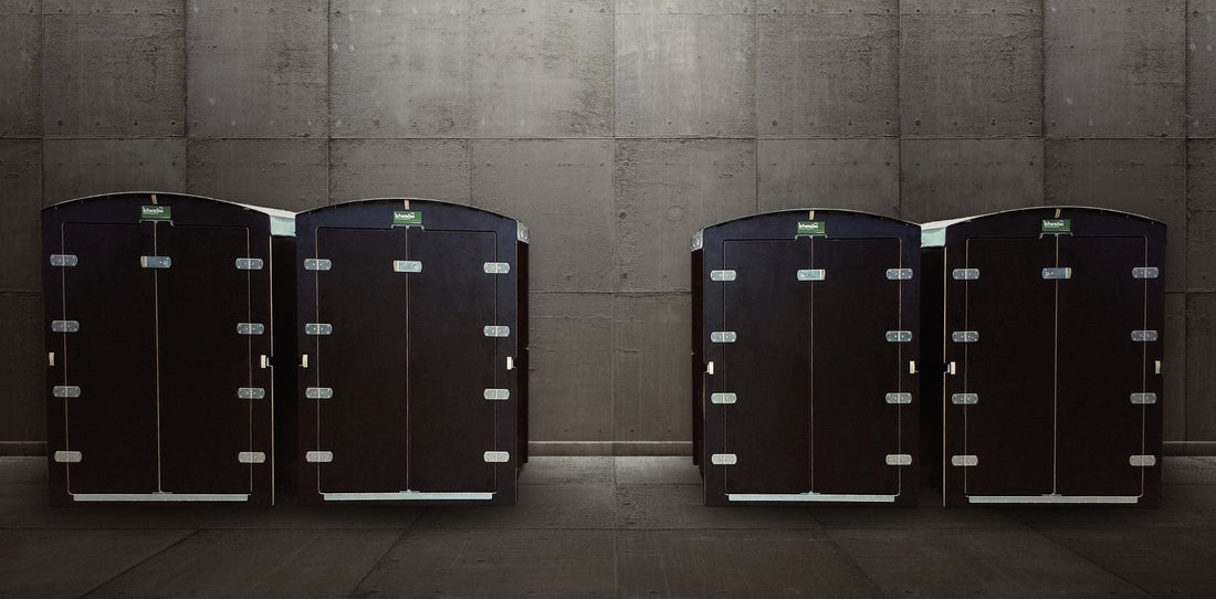 Vier schwarze Stahlkisten mit silbernen Scharnieren vor grauer Betonwand im Lagerraum