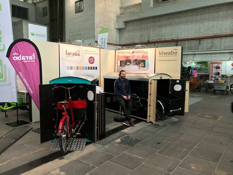 Messestand mit Fahrradboxen Farabo und Kiwabo auf Fahrradmesse in Berlin, Mann sitzt dazwischen