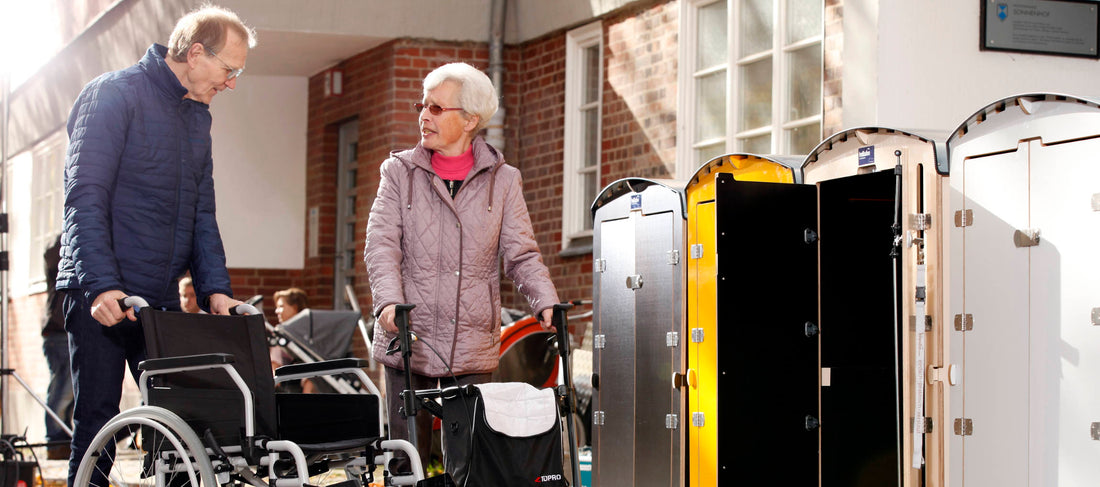 Seniorenpaar mit Rollstuhl und Rollator vor Pflegeschrank im Außenbereich eines Pflegeheims