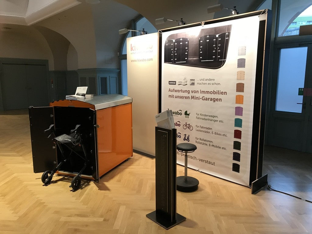 Ausstellungsstand mit orangefarbener Mini-Garage für Rollatoren und Fahrräder auf Immobilienkongress