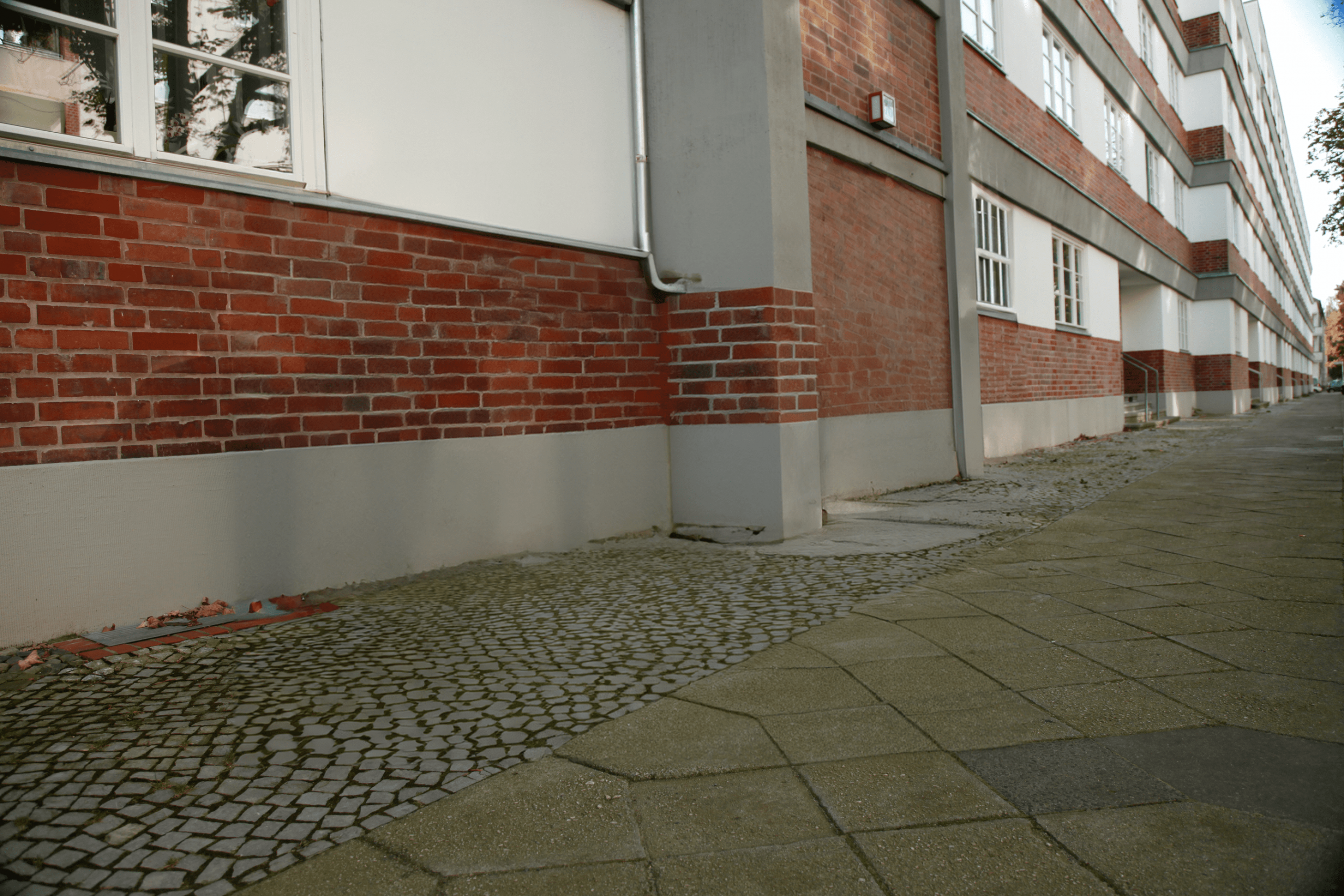Rote Backsteinfassade mit Fenstern und Gehweg, ideal für Fahrradaufbewahrung