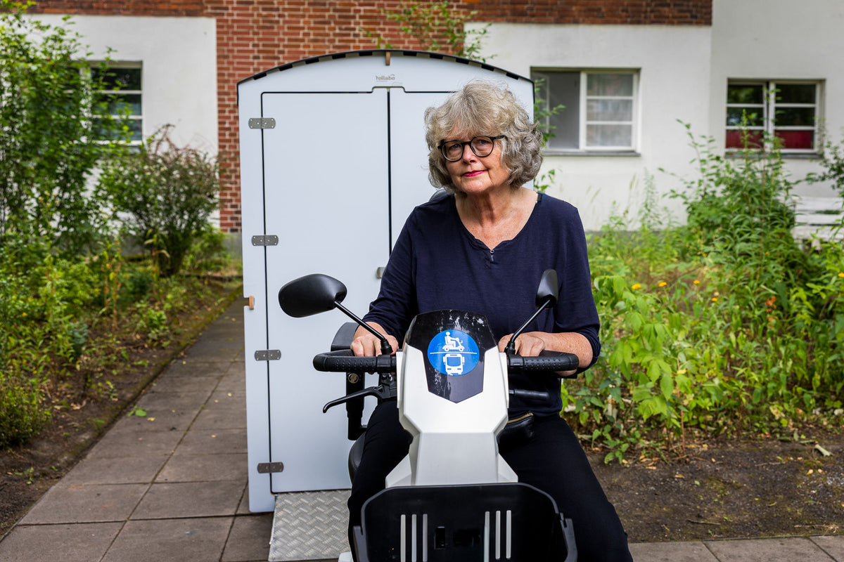 Seniorin mit E-Mobil an einer weißen rollabo Box