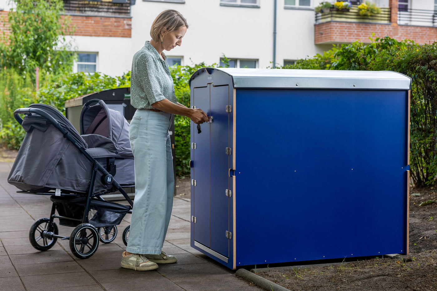 Frau mit Kinderwagen an blauer kiwabo Box im Innenhof