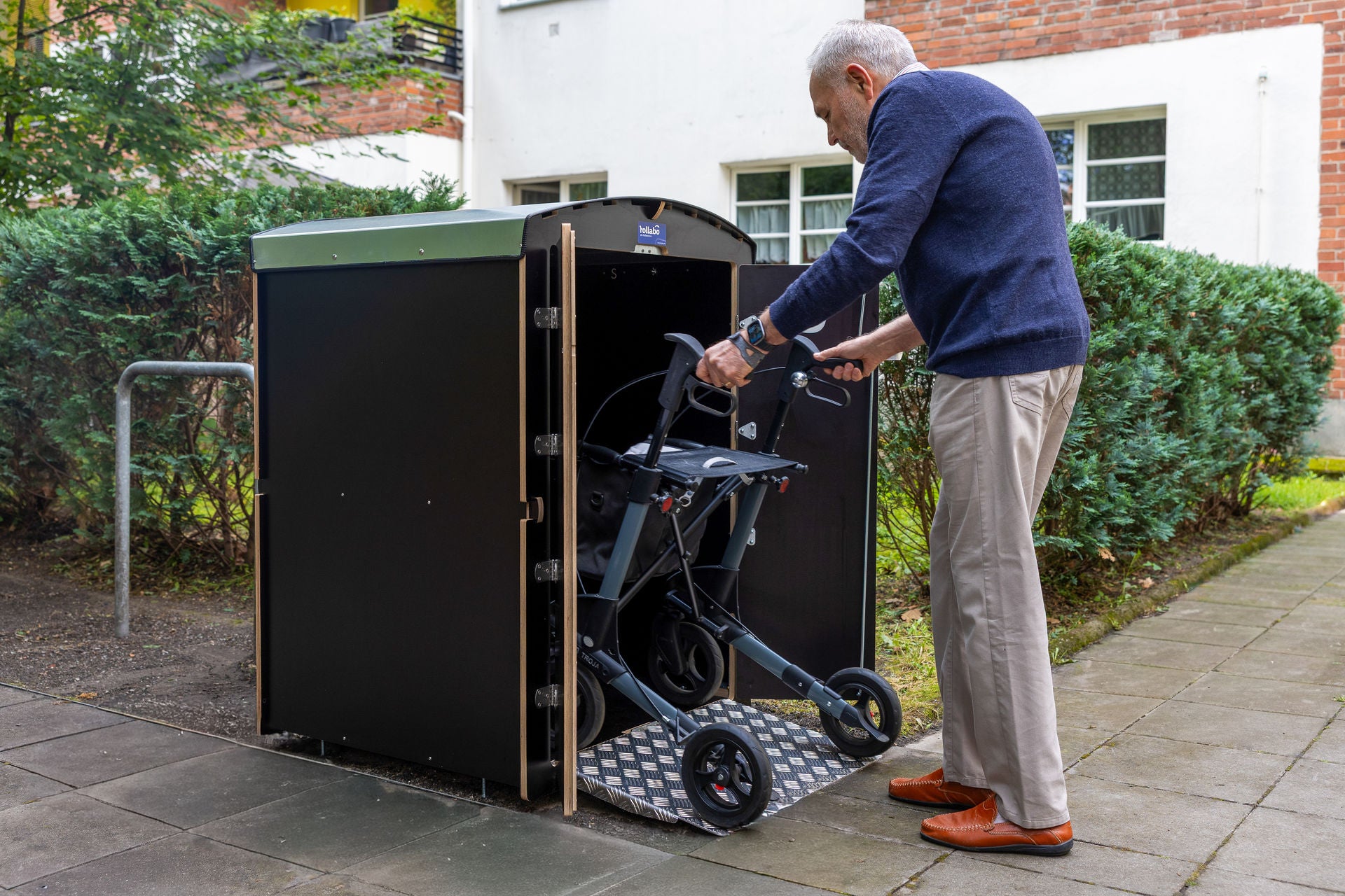 Senior stellt Rollator in eine schwarze rollabo Box, Wohnanlage
