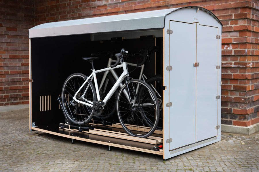 Weiße farabo Fahrradbox, geöffnet, mit Rennrad vor Backsteinwand