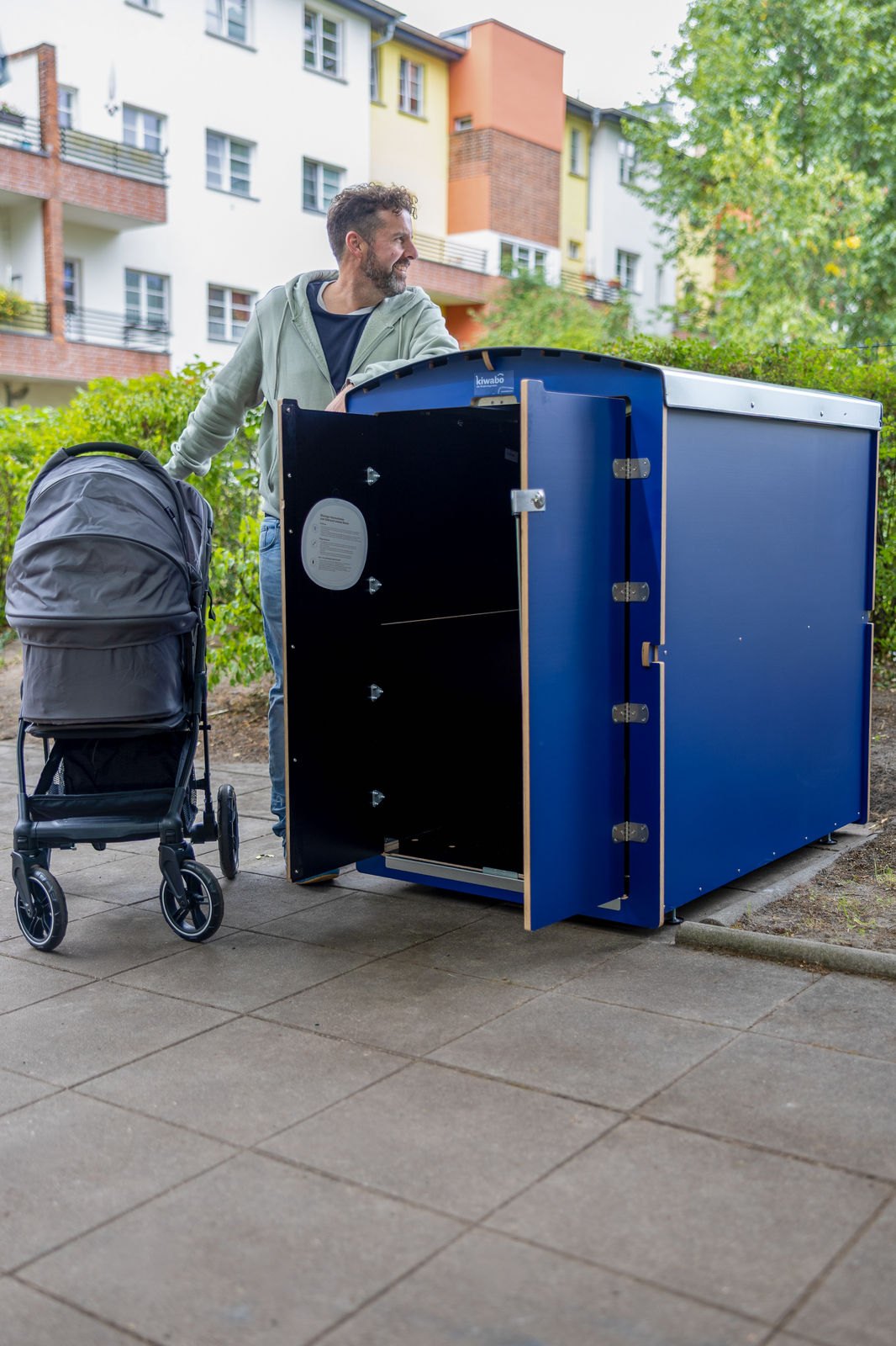 Mieter mit Kinderwagen an einer blauen kiwabo Kinderwagenbox vor einer Wohnanlage