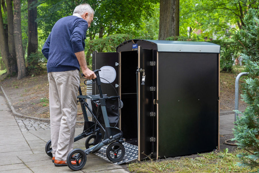 Senior stellt Rollator in eine schwarze rollabo Rollatorbox in einer Wohnanlage