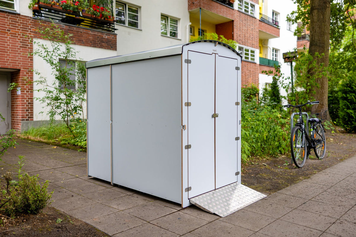 Weiße rollabo Box vor einer Wohnanlage mit Backsteinfassade