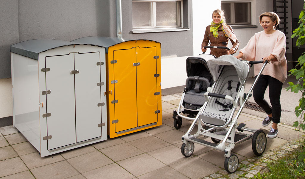 Zwei Frauen mit Zwillingskinderwagen vor weißen und gelben Müllbehältern in modernem Wohnumfeld