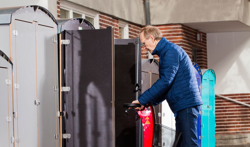 Mann in blauer Jacke schließt E-Bike in modernen, bunten Fahrradboxen ab, urbaner Hintergrund