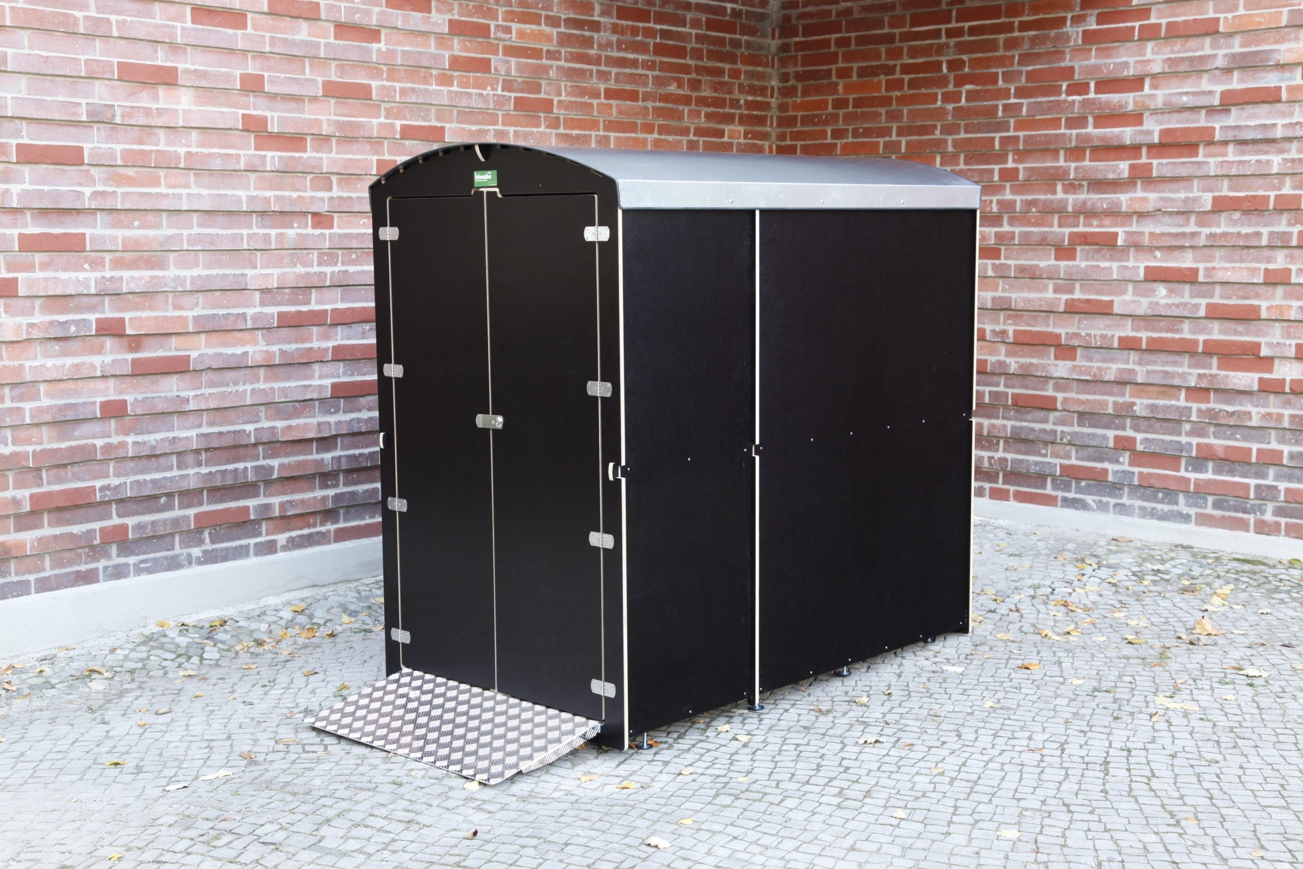 Große diebstahlsichere Aufbewahrungsbox für Rollatoren mit Rampe vor Ziegelwand